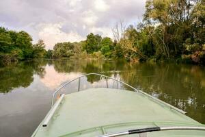 a boat on a river with trees and a cloudy sky photo