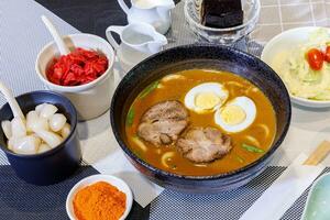 Japanese curry with udon noodle and crispy pork chop croquettes and boiled egg topping on bowl cup style. photo