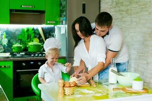 happy family mom and little son and dad are preparing dough in kitchen at table. products for dough are on table photo