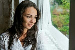 cute woman sitting on the windowsill and looking out the window photo