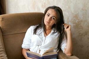 mujer sentado en un silla participación un libro en su mano, estilo de vida concepto foto