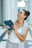 Confident young woman laughing and carrying notepad in hand while standing photo
