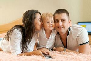 happy family lying on the bed and hugging, mom dad and little son photo
