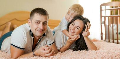 contento familia acostado en el cama y abrazando, mamá papá y pequeño hijo foto