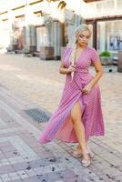 beautiful woman with long braid in pink dress with white polka dots posing on street in the city photo