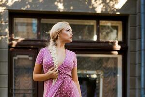 beautiful woman with long braid in pink dress with white polka dots posing on street in the city photo