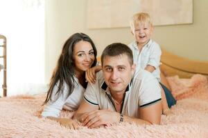 contento familia acostado en el cama y abrazando, mamá papá y pequeño hijo foto