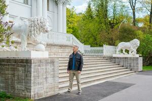 a man in casual clothes stands near a beautiful white building with lions photo