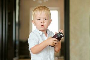 un pequeño chico soportes en el habitación y sostiene un juguete coche en su manos foto