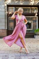 beautiful woman with long braid in pink dress with white polka dots posing on street in the city photo