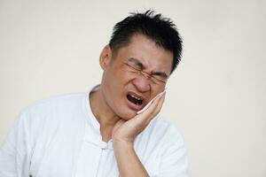 Asian man suffers from  painful toothache, gum inflammation, use hand to touch his cheek, close eyes, open mouth. Concept, dental health problem and health care. photo