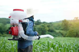 Asian man farmer carry fertilizer sprayer machine on back, stand at garden. Concept, farmer use engine facilitator tool in agriculture. Easy and fast for sowing. photo