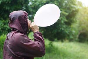 asiático hombre es soplo, inflar aire dentro un globo en el parque. concepto, preparar globo para jugando juegos como un juguete, Decorar fiesta o celebracion. recreación o ocio actividad. divertido y contento tiempo. foto