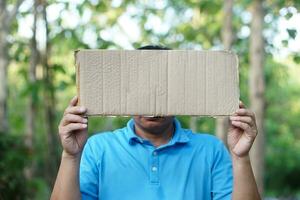 Man wears blue shirt, holds blank paper card board for adding texts or words. Concept, protest. Sign and notice. Announcement. Giving information photo