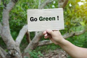 Hands hold paper sign with text  Go Green in forest. Concept, campaign people around the world to stop activities that can cause global warming. Do eco friendly activity. Environment conservation. photo