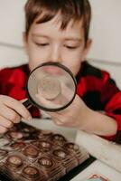 collecting coins. The boy examines an old coin through a magnifying glass. Dollars, euros on the table. Money of different nations. Savings in the form of currencies and coins photo