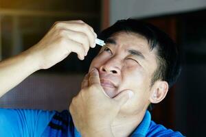 Asian man uses artificial tear lubricant eye drops with his eyes. Concept, Healthcare. Treatment for dry eye symptoms, eye inflammation diseases. Relief irritated optics. photo