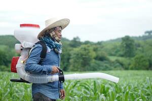 Asian man farmer carry fertilizer sprayer machine on back, stand at garden. Concept, farmer use engine facilitator tool in agriculture. Easy and fast for sowing. photo