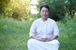 asiático mujer budista usa blanco traje, hacer meditación sentado a tranquilo bosque. concepto, cultura de fe. religioso actividad. paz de mente gestión. hacer concentración. foto