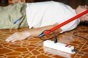 Using red plastic stick is moving away the electric plug socket from the unconscious man who lay down on the floor. Concept, Electric Shock. Emergency basic rescue. First Aid photo