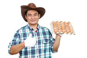 Handsome Asian man wears hat, plaid shirt, holds tray of eggs, isolated on white background. Concept, Organic agricultural farming, Farmers produce healthy eco food. Best food during bad economy. photo