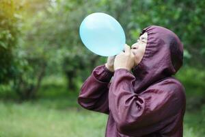 Asian man is blowing, inflating air into a balloon in the park. Concept, prepare balloon for playing games as a toy, decorate party or celebration. Recreation or leisure activity. Fun and happy time. photo