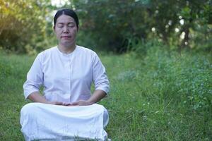 Asian woman Buddhist wears white costume, do meditation sitting at tranquil forest. Concept, culture of faith. Religious activity. Peace of mind management. Make concentration. photo