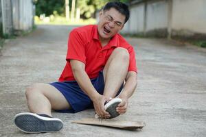 Asian man sits on floor, feels hurt after steped on nails. Concept, unsafe , risk for dangerous tetanus. Be careful and look around during walking  on the floor or risk places. Accident insurance. photo