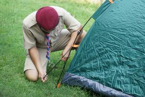 Thai boy scout is setting up the tent at campsite for camping outdoor. Concept, pitching camping tent, accomodation for temporary outdoor sleeping as scout hiking activity. photo