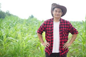 Handsome Asian man farmer wears hat, red plaid shirt, pose hand on waist. Concept, agriculture occupation. Farmer visits garden to take care crops. Thai farmer lifestyle. photo