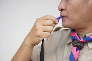 Close up man wears boy scout uniform is blowing the whistle. Concept, Scout blow whistle as meaningful sign for doing activity to assembly, start competition or playing games in scout lesson. photo