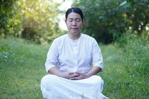 asiático mujer budista usa blanco traje, hacer meditación sentado a tranquilo bosque. concepto, cultura de fe. religioso actividad. paz de mente gestión. hacer concentración. foto