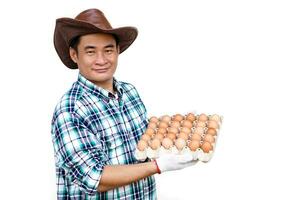 Handsome Asian man wears hat, plaid shirt, holds tray of eggs, isolated on white background.  Concept, Organic agricultural farming, Farmers produce healthy eco food. Best food during bad economy. photo