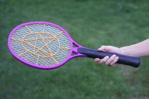 Closeup hand holds mosquito electric swatter racket. Concept, electric device to kill mosquitoes, insects, bugs by swatting to flying insects. photo