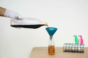 Close up hand holds bottle of soft drinks water to pour into the funnel bottle for doing science experiment.Concept, Science process about reaction of chemical substance. photo
