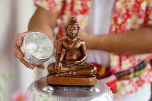 cerca arriba mano sostiene tailandés tradicional plata cuenco a verter agua en el Buda estatua en Songkran día a Adoración y hacer deseos para el prosperidad. concepto, cultura de fe. religioso ceremonia para suerte foto