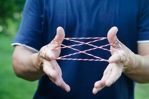 Closeup boy hands is playing rope which called cats cradle game. Concept, game involving the creation of various style figures between the fingers. Traditonal playing. photo