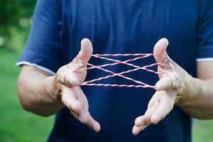 Closeup boy hands is playing rope which called cats cradle game. Concept, game involving the creation of various style figures between the fingers. Traditonal playing. photo