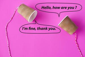 Paper cups with string on pink background. Bubble speech with words. Hello, How are you  I'm fine, thank you. Concept, English conversation. Teaching aid. Cummunication. photo