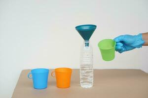 Close up hands holds green mug to pour water into bottle. Doing experiment. Concept, water quantity measurement for mixing chemical substances. Learning by doing. photo