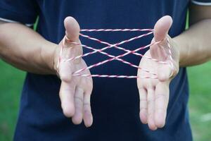 Closeup boy hands is playing rope which called cats cradle game. Concept, game involving the creation of various style figures between the fingers. Traditonal playing. photo