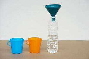 Blue and orange cups , bottle of water and funnel on the top. Concept, equipment for doing experiment, measuring liquid quantity. photo