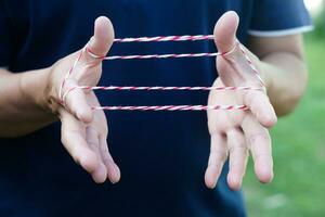 Closeup boy hands is playing rope which called cats cradle game. Concept, game involving the creation of various style figures between the fingers. Traditonal playing. photo