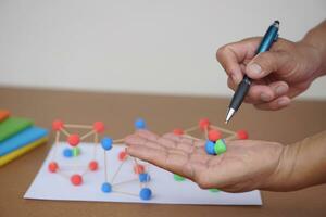 Close up teacher hands holds pen and plasticine balls to teach about basic molecule structure in chemist lesson. Concept, science education. Describing and analyzing. photo