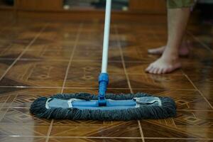 cerca arriba hombre utilizar un fregona a fregona el piso. concepto, casa faena en diario vida. higiénico y sanitario. fregona el polvo, limpiar el piso. limpieza casa. mantener loseta pisos a ser limpiar y brillante foto