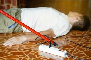 Using red plastic stick is moving away the electric plug socket from the unconscious man who lay down on the floor. Concept, Electric Shock. Emergency basic rescue. First Aid photo