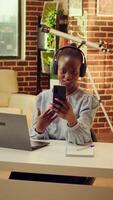 vertical vídeo trabalhador autonomo em Video chamada às casa discutindo sobre maneiras para terminar conectados tarefas, atendendo teleconferência conexão em Smartphone às escrivaninha. mulher usando rede ligar para presente e o negócio