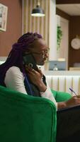 Vertical video Worker managing bookings by phone, answering calls to register to clients for room reservation and writing personal information on clipboard. Hotel staff taking notes using telephone