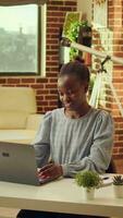 verticale video casa basato africano americano sviluppatore inizia giorno di soluzione Compiti per in linea networking lavoro. donna libero professionista utilizzando il computer portatile a stazione di lavoro per rispondere per e-mail, naturale leggero a