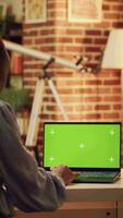 verticaal video vrouw looks Bij groene scherm Aan Scherm en werken Aan online carrière taken voor freelancer functie, blanco mockup scherm Aan laptop. telewerker toepassingen pc met geïsoleerd kopieerruimte. statief schot.